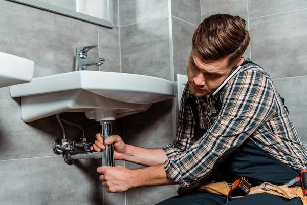 Instalador Tocando Tubo Enquanto Fala Smartphone Banheiro — Fotografia de Stock