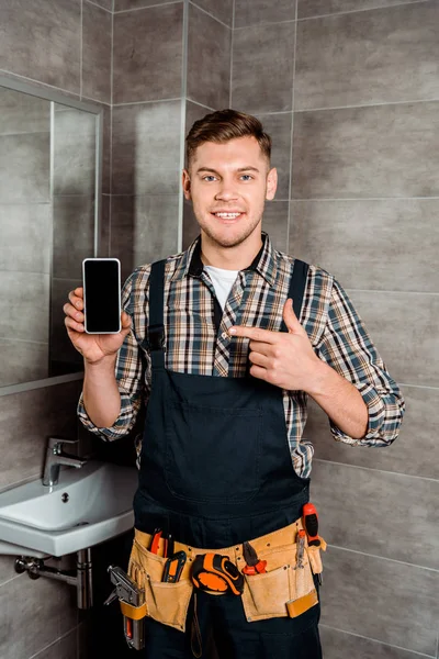 Šťastný Instalátor Ukazuje Prstem Smartphone Prázdnou Obrazovkou Koupelně — Stock fotografie