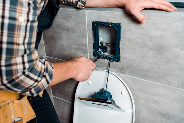 cropped view of installer holding screwdriver near toilet 