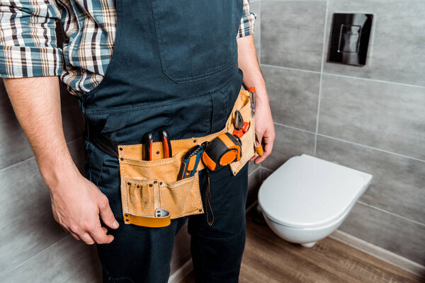 cropped view of installer with tool belt standing near toilet 