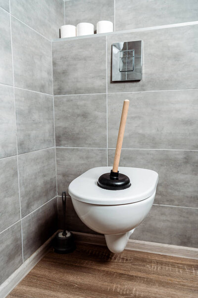 plunger on white toilet near toilet paper rolls 