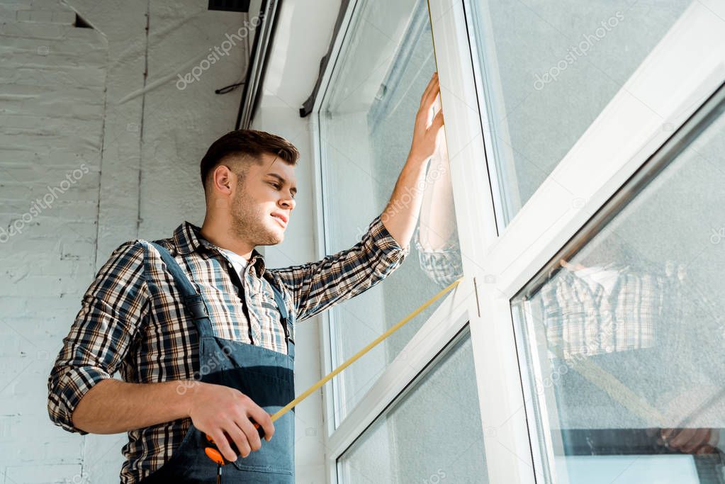 low angle view of installer standing near windows and holding measuring tape