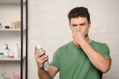 Deodorant tutarken burun tıkayan hoşnutsuz genç adam.