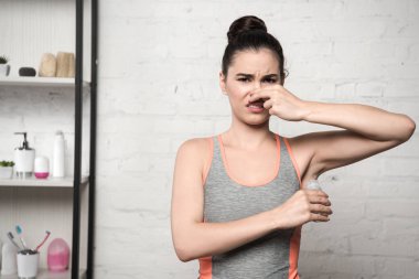 Şok olmuş bir kadın koltuk altına deodorant sıkarken eliyle burnunu tıkamış.