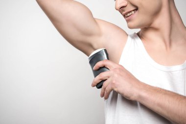 cropped view of smiling man applying deodorant on underarm isolated on grey clipart