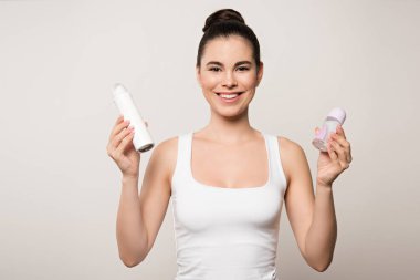 Gri renkte deodorantları tutan neşeli kadın kameraya gülümsüyor.