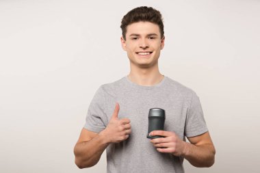 Gri tişörtlü gülümseyen adam elinde deodorant tutuyordu ve baş parmağını gri üzerinde gösteriyordu.