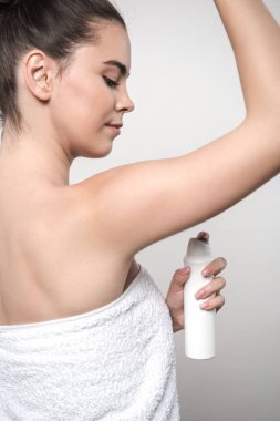 Deodorant süren genç bir kadın gri üzerine izole edilmiş.