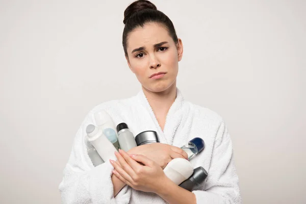 Niezadowolona Kobieta Szlafroku Trzyma Różne Dezodoranty Patrząc Kamerę Odizolowaną Szaro — Zdjęcie stockowe