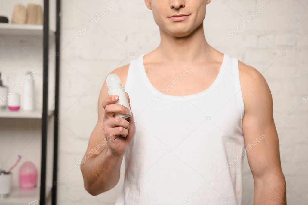 cropped view of young man in white sleeveless shirt holding deodorant