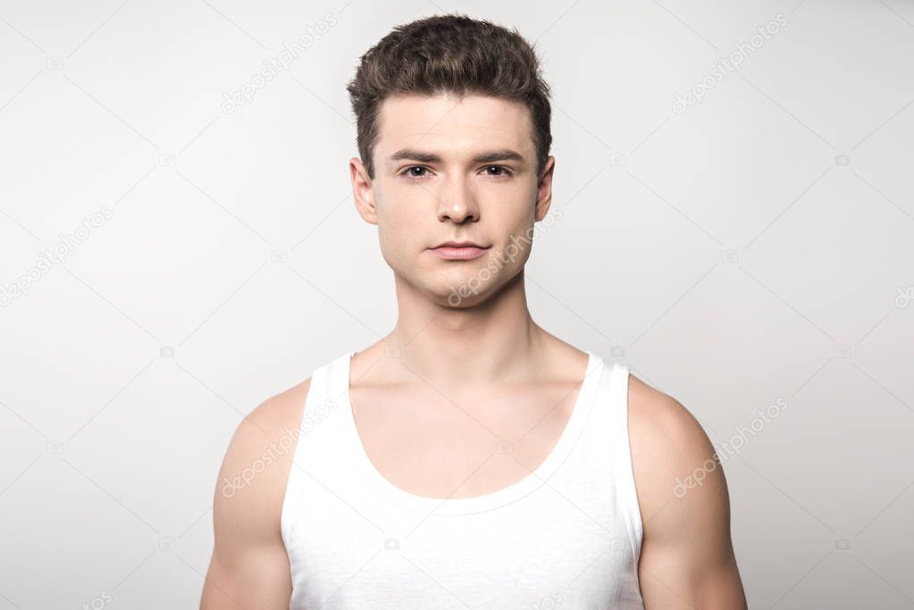 handsome man in white sleeveless shirt looking at camera isolated on grey