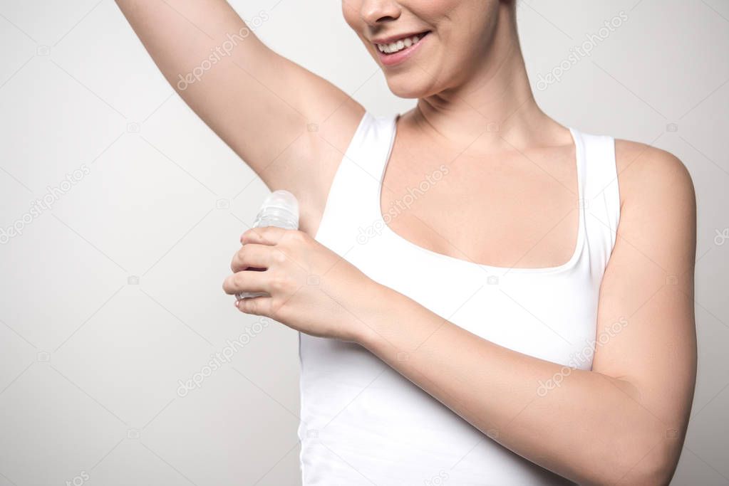 cropped view of smiling woman applying deodorant on underarm isolated on grey