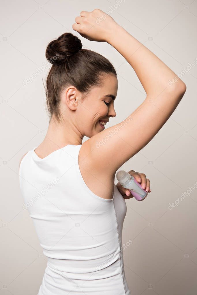 happy woman applying deodorant on underarm isolated on grey