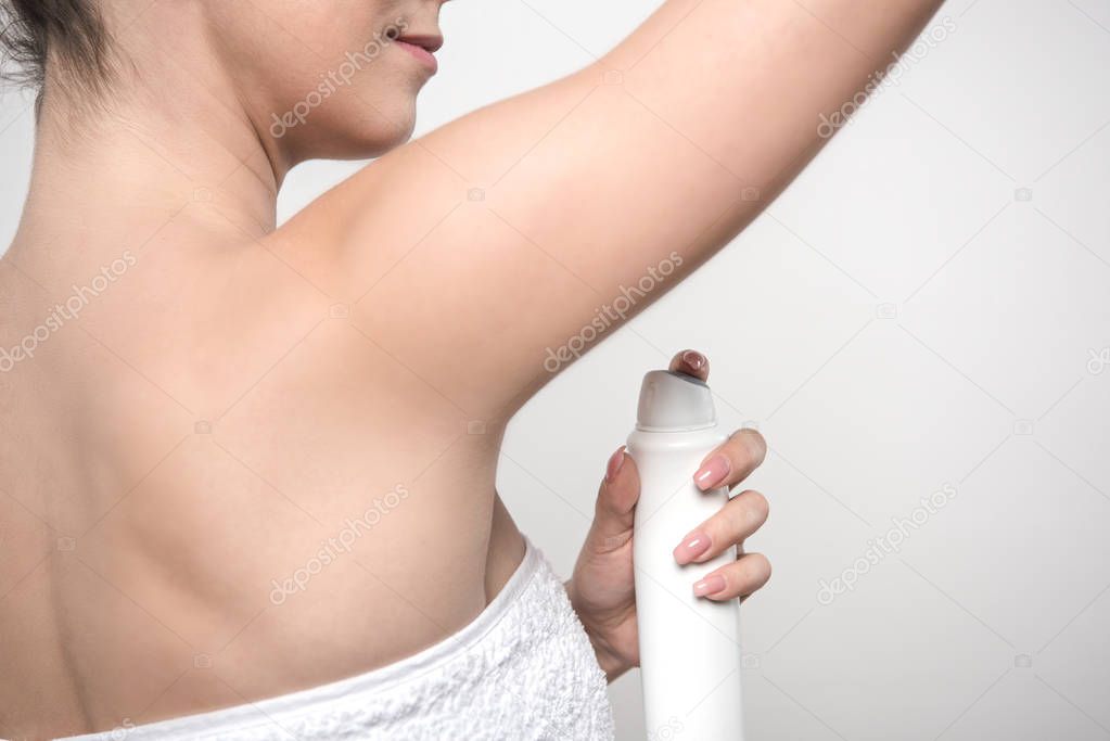 partial view of young woman applying deodorant on underarm isolated on grey
