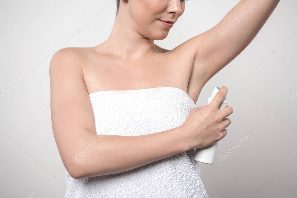 cropped view of young woman applying deodorant on underarm isolated on grey