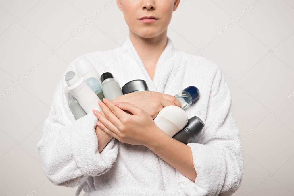 partial view of woman in bathrobe holding different deodorants isolated on grey