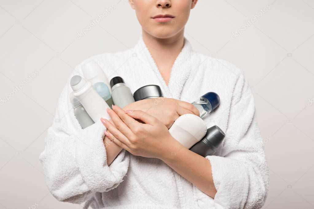 partial view of woman in bathrobe holding different deodorants isolated on grey