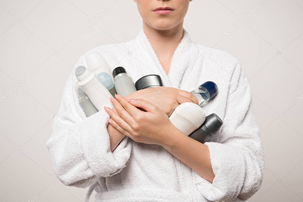 cropped view of woman in bathrobe holding different deodorants isolated on grey