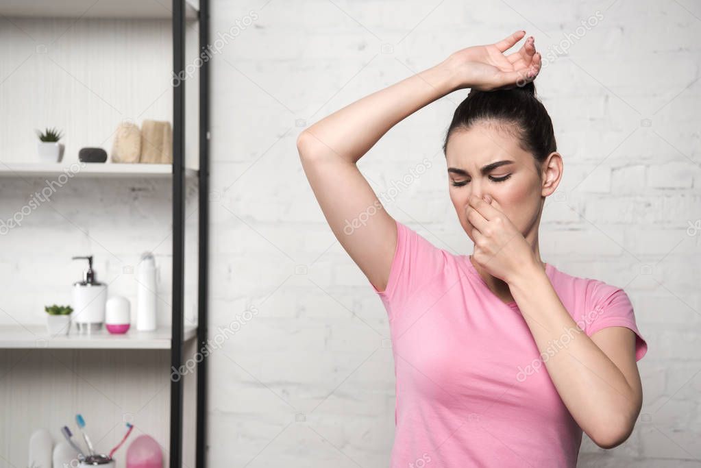 shocked woman plugging nose with hand while looking at underarm