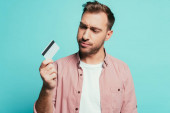 Frustrierter Mann mit Kreditkarte, isoliert auf blauem Grund