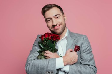 Kırmızı güller tutan takım elbiseli yakışıklı adam, pembe üzerine izole edilmiş.
