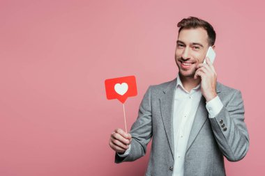 Sevgililer günü için kalbi olan mutlu bir adam akıllı telefonuyla konuşurken pembe bir kart tutuyor. 