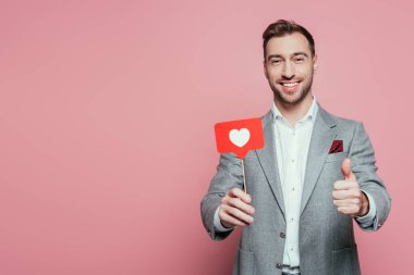 Sevgililer günü için başparmağıyla kart tutan mutlu bir adam. Pembe renkte izole edilmiş. 