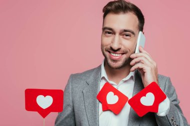 Akıllı telefondan konuşan mutlu bir adam ve sevgililer günü için kalpli kartlar tutan, pembe renkte izole edilmiş bir adam. 