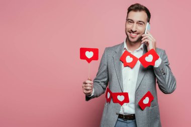 Akıllı telefondan konuşan ve sevgililer günü için kalplerle dolu kartlar tutan neşeli bir adam. Pembe renkte izole edilmiş. 