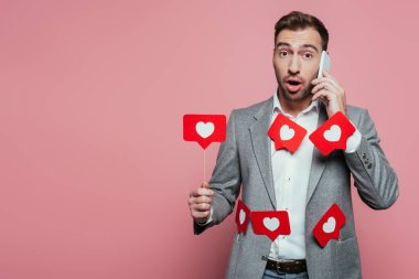 Akıllı telefondan konuşan yakışıklı bir adam ve sevgililer günü için kalplerle dolu kartlar tutan pembe bir adam. 