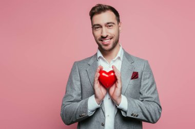Sevgililer günü için kırmızı kalbi tutan mutlu adam, pembe üzerine izole edilmiş. 