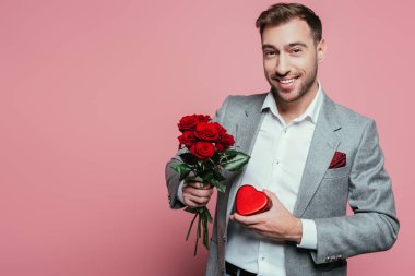 Sevgililer günü için kalp hediye kutusu ve gül buketi tutan mutlu adam, pembe renkte izole edilmiş.