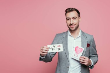 Yakışıklı sakallı adam elinde iki tane sevgililer günü kartı tutuyor, pembe üzerinde izole edilmiş.