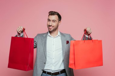 happy positive man holding shopping bags, isolated on pink clipart
