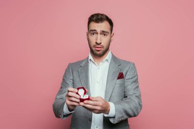 Elinde evlilik yüzüğü olan kafası karışmış bir adam, pembe bir kutuda izole edilmiş.