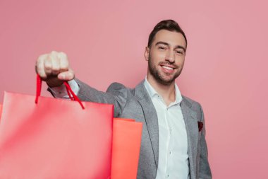 Alışveriş torbaları taşıyan neşeli adam, pembe üzerinde izole edilmiş.