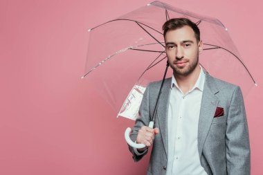Şemsiye tutan yakışıklı sakallı adam, pembe üzerine izole edilmiş.