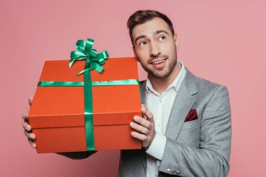 Gülümseyen adam elinde büyük bir hediye kutusu tutuyor, pembe üzerinde izole edilmiş.
