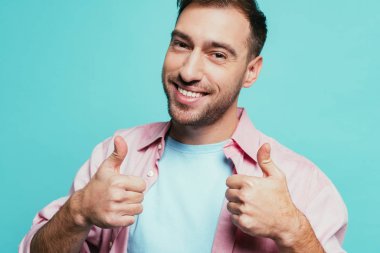 Neşeli yakışıklı adam başparmak kaldırıyor, mavi üzerine izole edilmiş.
