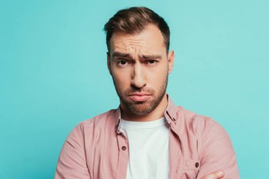 Kuşkucu yakışıklı adam kameraya bakıyor, mavi üzerine izole edilmiş.