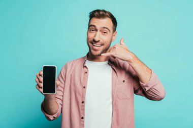 Neşeli yakışıklı adam bana işaret ver. Akıllı telefon, boş ekran, mavi üzerine izole edilmiş.