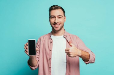 Neşeli bir adam baş parmağını gösteriyor ve telefonuyla boş ekranı var, mavi ekranda izole edilmiş.