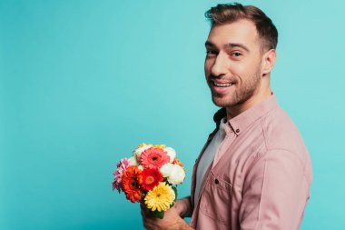 Sakallı mutlu adam elinde bir buket çiçek tutuyor, maviden soyutlanmış.