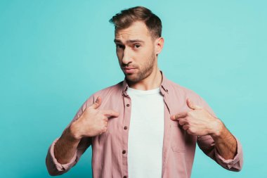 duygusal yakışıklı adam kendini işaret ediyor, mavi üzerine izole edilmiş.