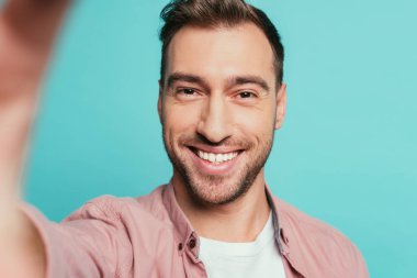 Yakışıklı, gülümseyen adam selfie çekiyor, maviden soyutlanmış.