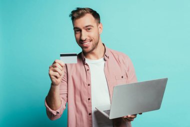 Sakallı adam internetten kredi kartı ve laptopuyla alışveriş yapıyor, mavi ile izole edilmiş.