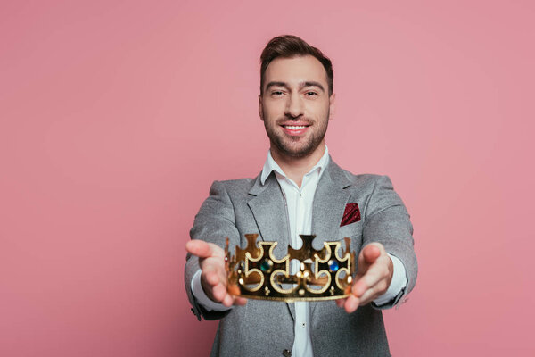 smiling bearded man in suit holding crown, isolated on pink