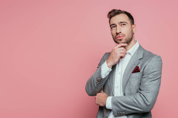 smiling bearded man thinking in grey suit, isolated on pink