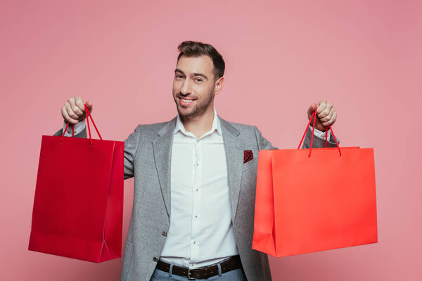 happy positive man holding shopping bags, isolated on pink
