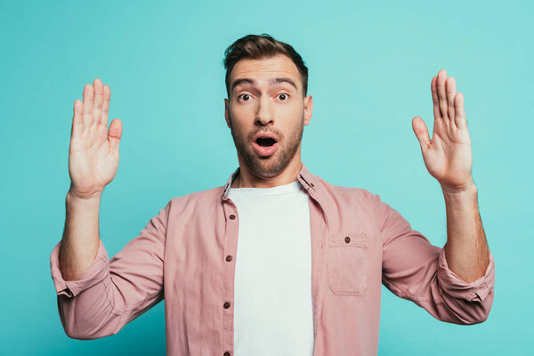 shocked handsome man with hands up, isolated on blue